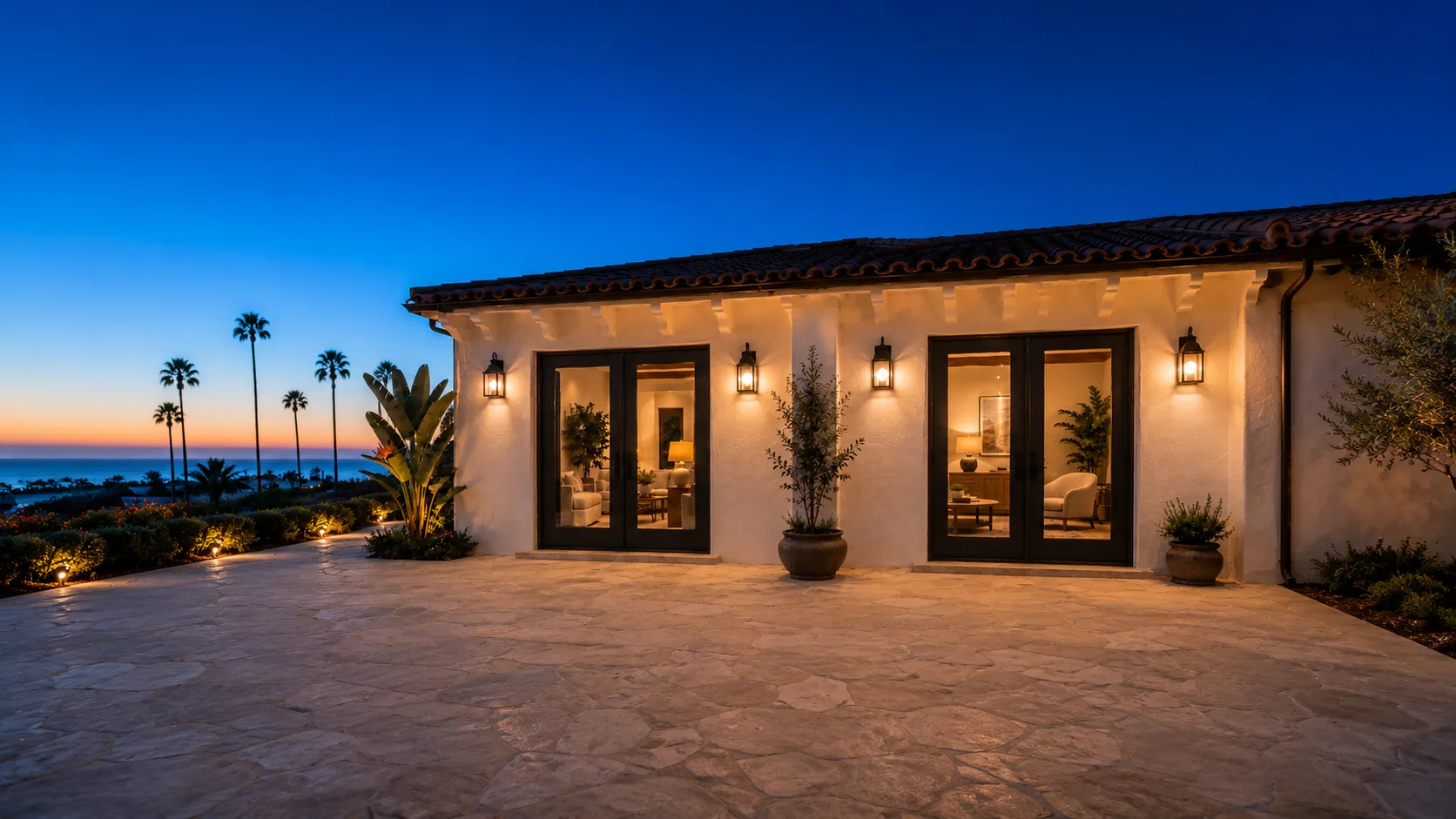 Exterior view of closed French doors with black iron hardware on white stucco coastal home at twilight
