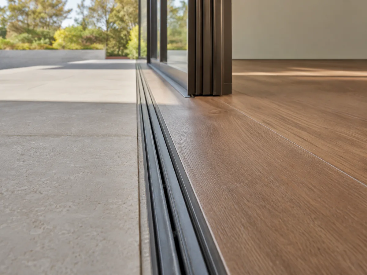 Flush threshold detail showing recessed multi-slide door track between interior hardwood and exterior patio stone
